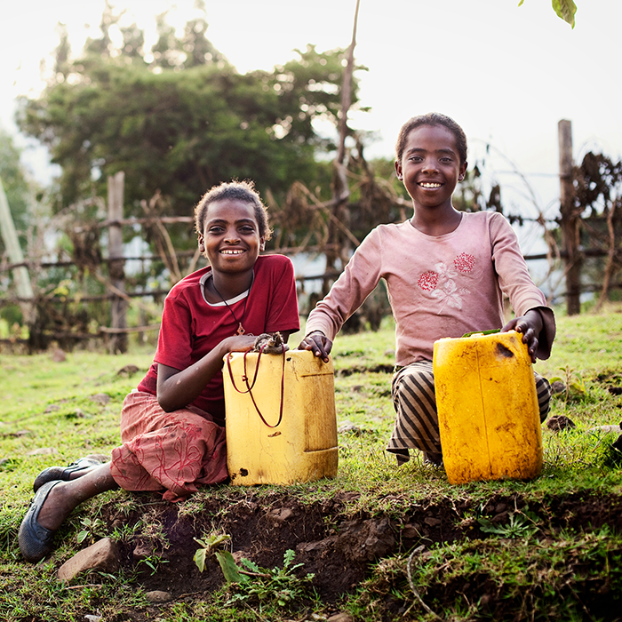 Two happy girls sitting with water jugs full of clean water